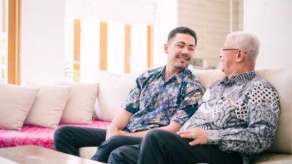 An elderly man and a younger man laughing together on a couch