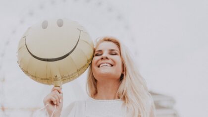 Blond woman is smiling and holding an emoji balloon