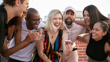 A group of friends laughing together and the girl in the middle is holding a cupcake