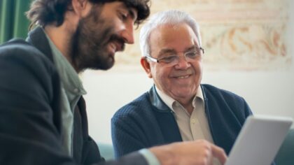 Two men smiling while looking at a computer screen