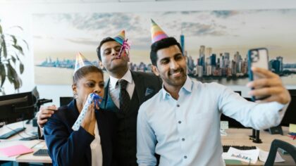 Three colleagues wearing party hats and taking a selfie