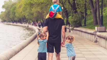Father is walking on the street with his 3 kids